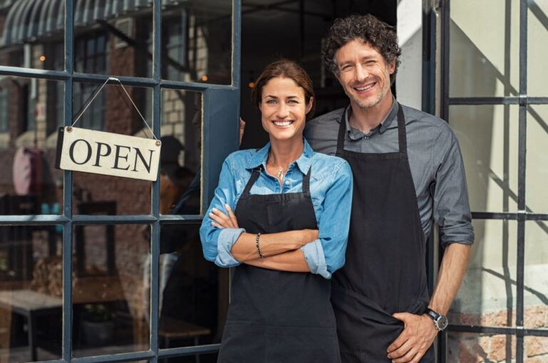 Couple standing outside their cafe with an open sign